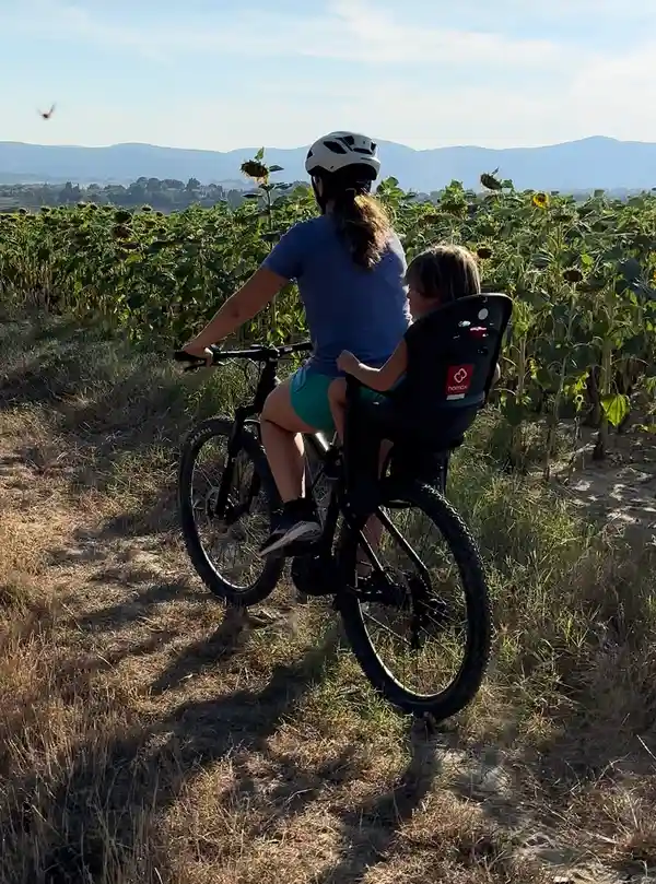 A woman cycling with a helmet, her child in the bike seat, among sunflowers